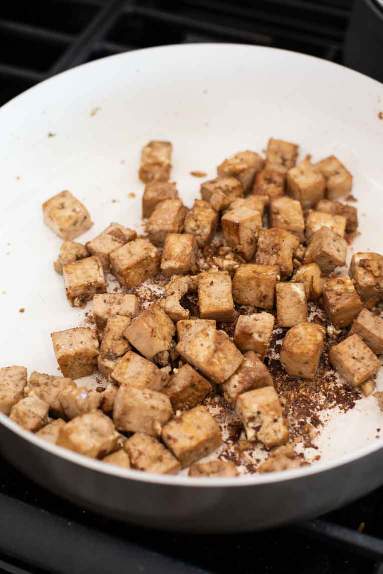Asian crispy tofu being cooked in a white pan.