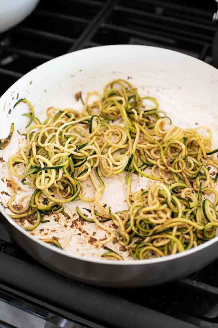 Zucchini noodles being cooked with soy sauce, ginger, and honey.
