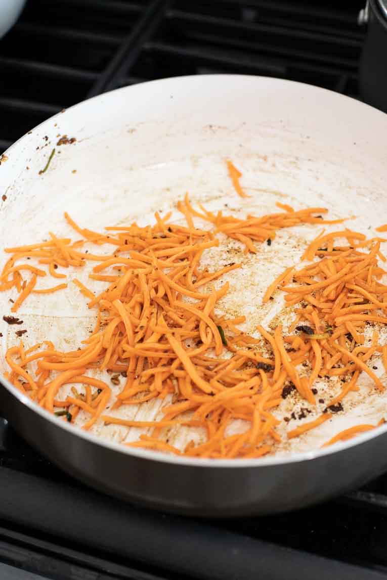 Sliced carrots being cooked in a frying pan.