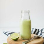 Close up of Creamy Avocado Lime Dressing in a glass jar next to a cut lime.
