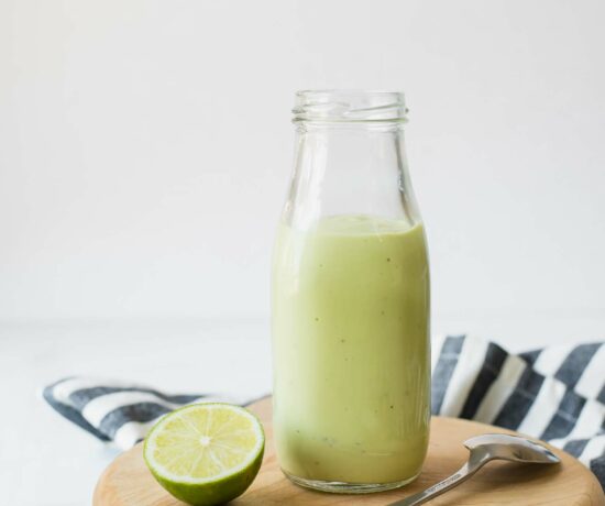 Close up of Creamy Avocado Lime Dressing in a glass jar next to a cut lime.