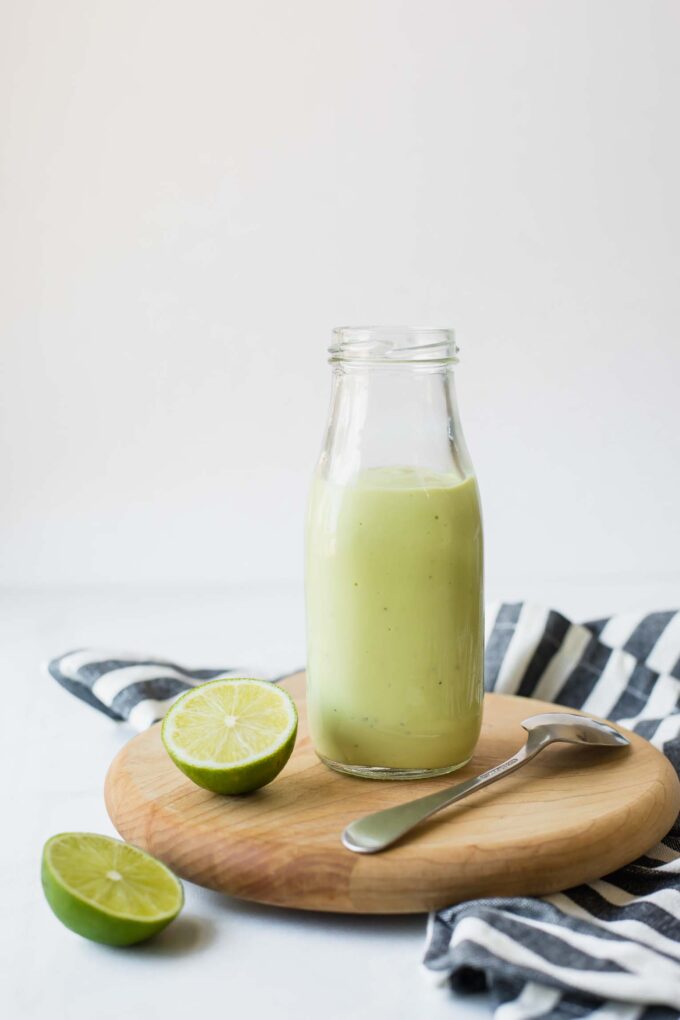 Close up of Creamy Avocado Lime Dressing in a glass jar next to a cut lime.