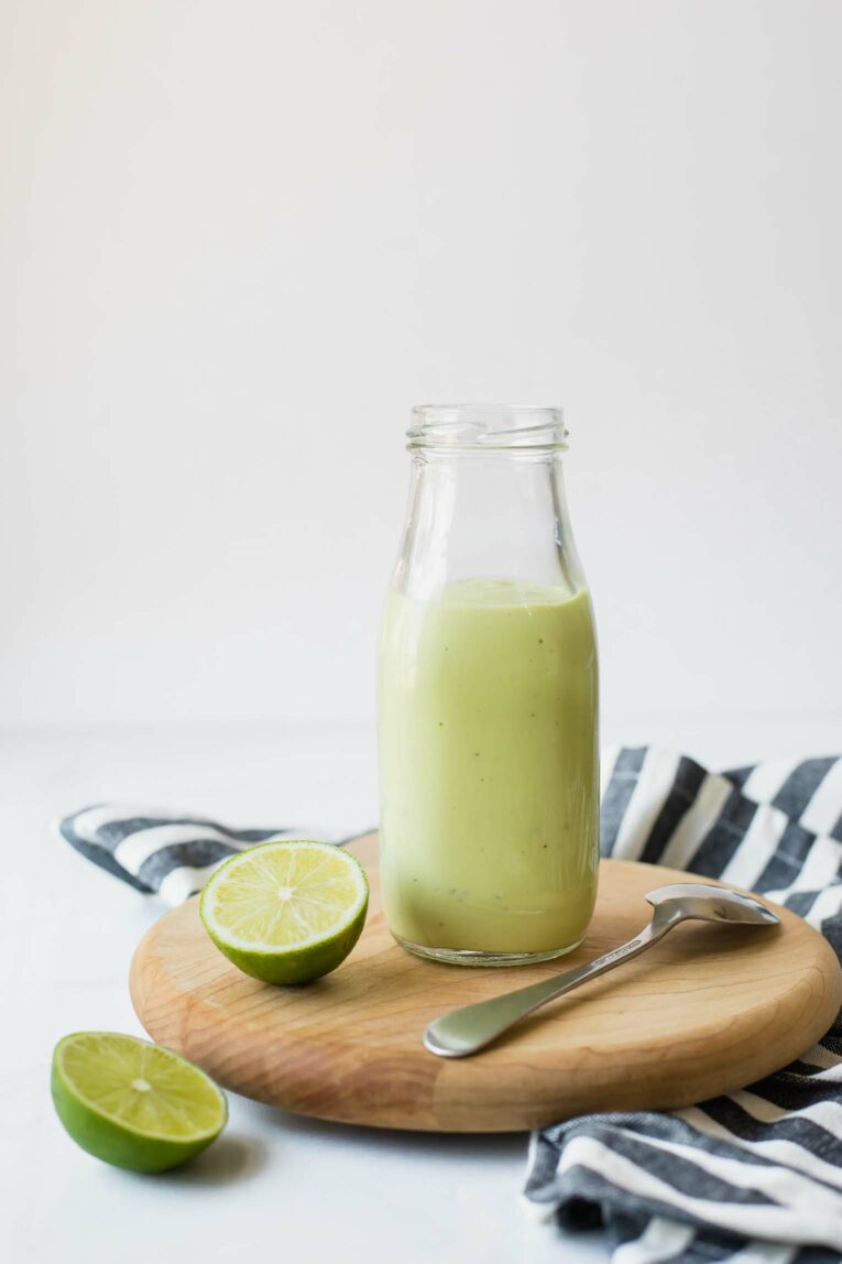 Close up of Creamy Avocado Lime Dressing in a glass jar next to a cut lime.