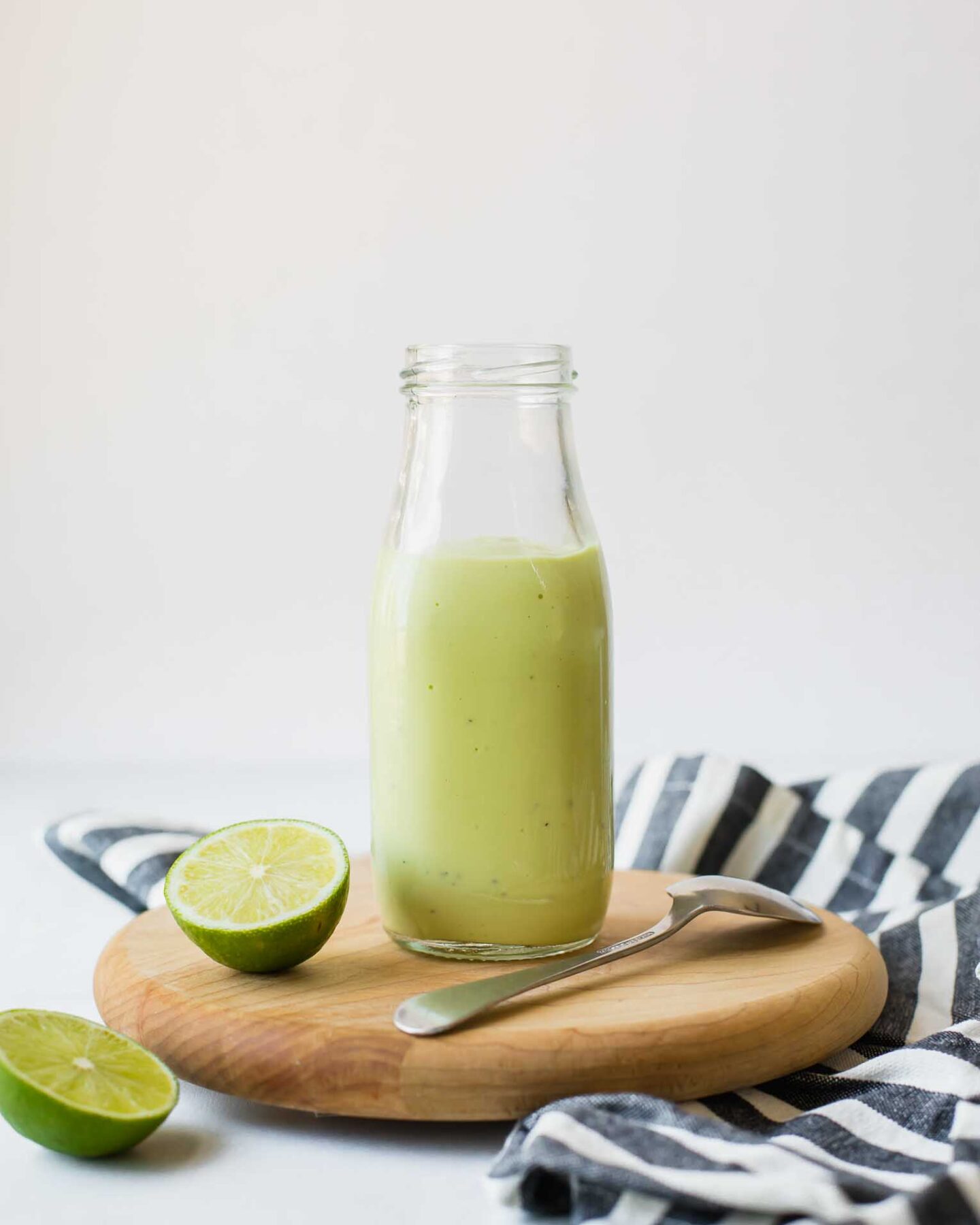 Creamy Avocado Lime Dressing in a glass jar with limes and a napkin.