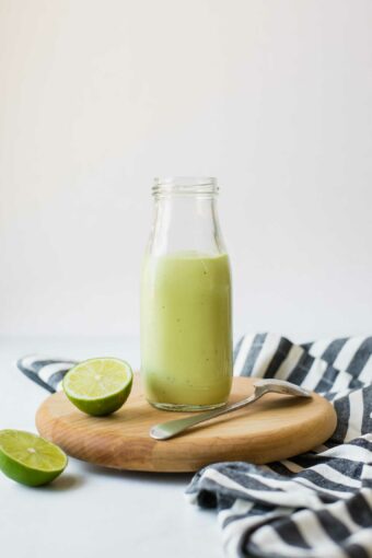 Creamy Avocado Lime Dressing in a glass jar with limes and a napkin.