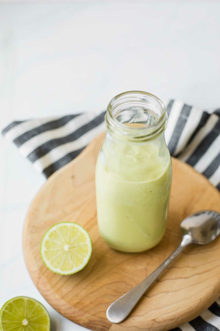 Angled shot of Creamy Avocado Lime Dressing on a wooden cutting board.