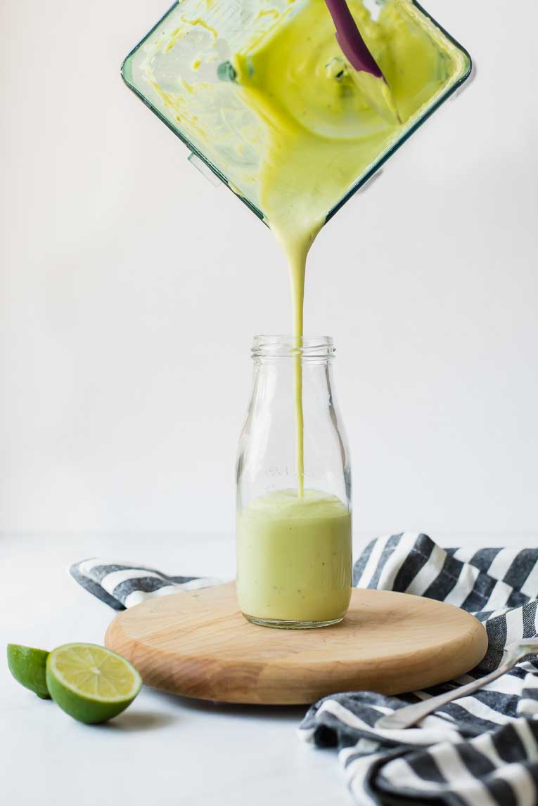 Creamy Avocado Lime Dressing being poured from a blender into a glass jar.
