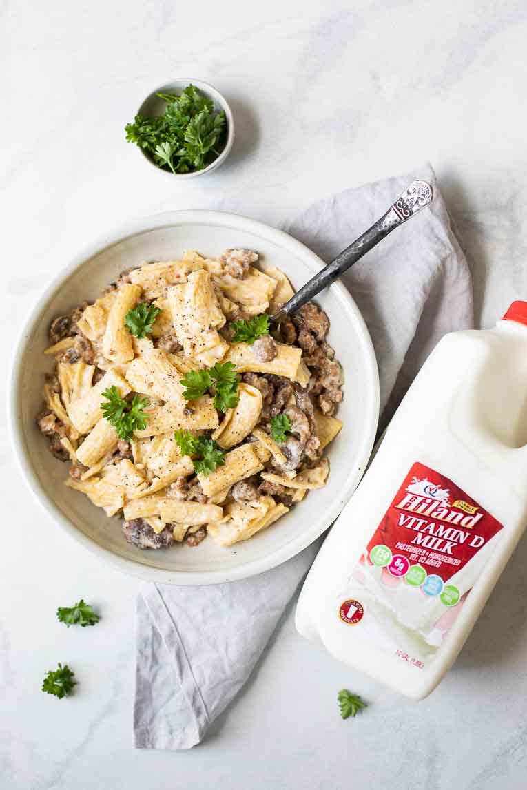 Top shot of white bowl of creamy sausage rigatoni next to Hiland Dairy milk.