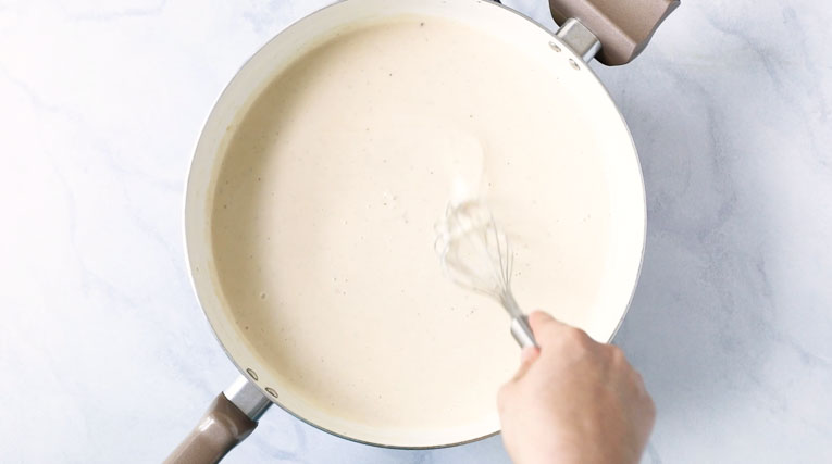 Creamy pasta sauce being whisked together in a pan.