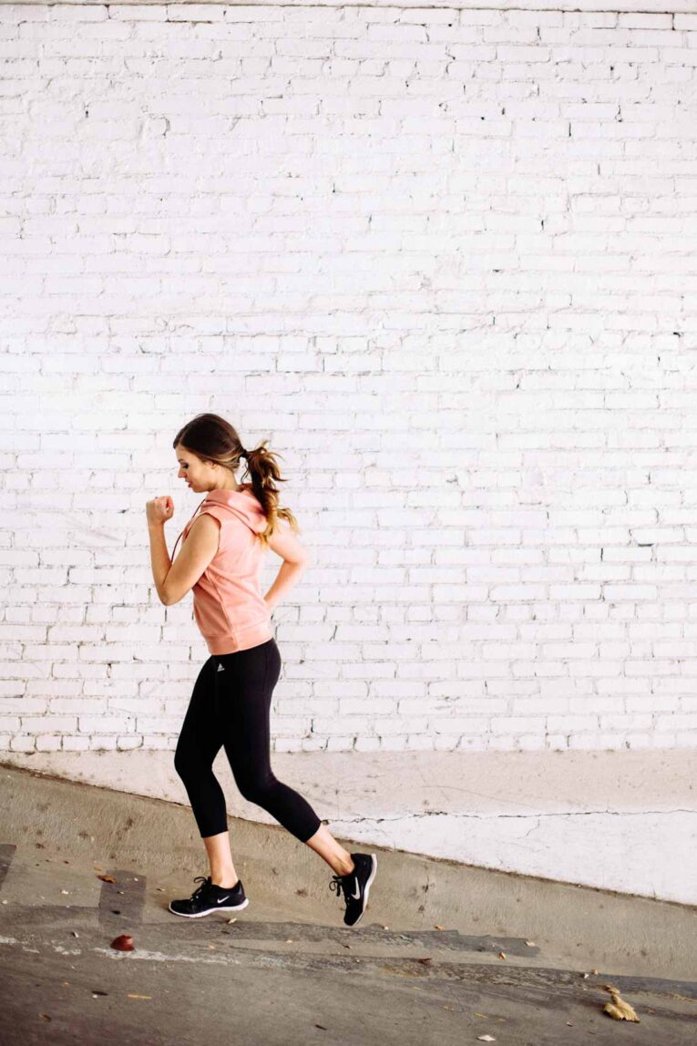 Woman running next to a white wall outside.