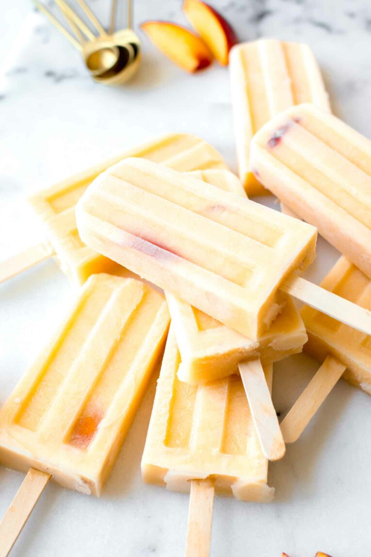 Side shot of Homemade Creamy Peach Popsicles on a marble countertop.