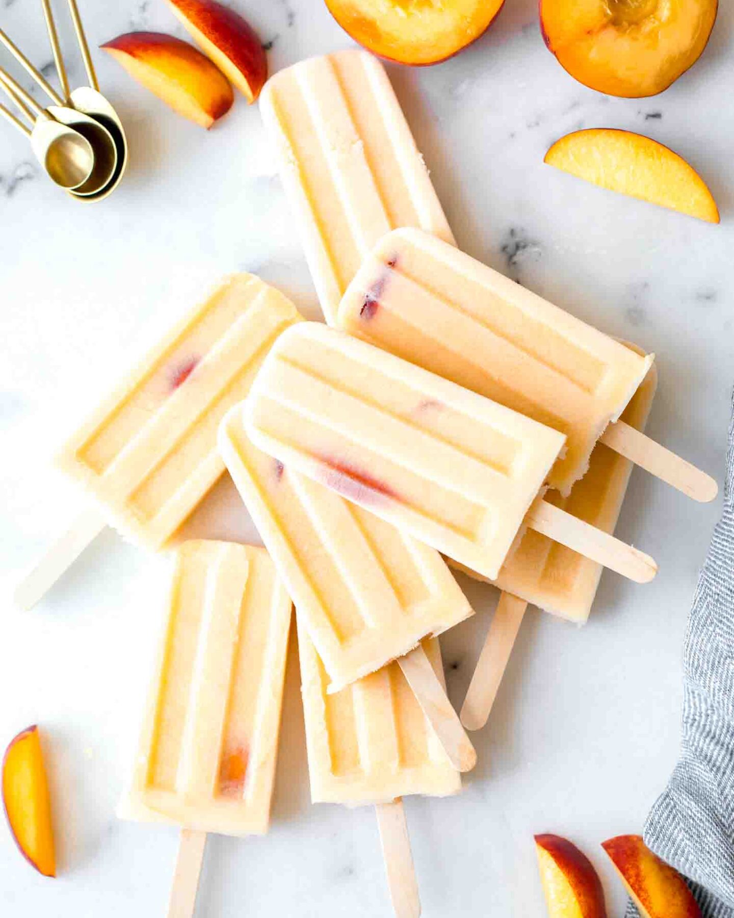 Top shot of Homemade Creamy Peach Popsicles, peach slices, and a napkin on a marble board.