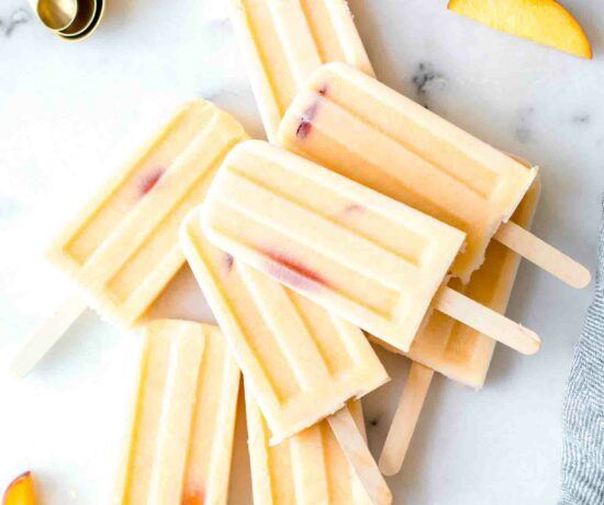 Top shot of Homemade Creamy Peach Popsicles, peach slices, and a napkin on a marble board.
