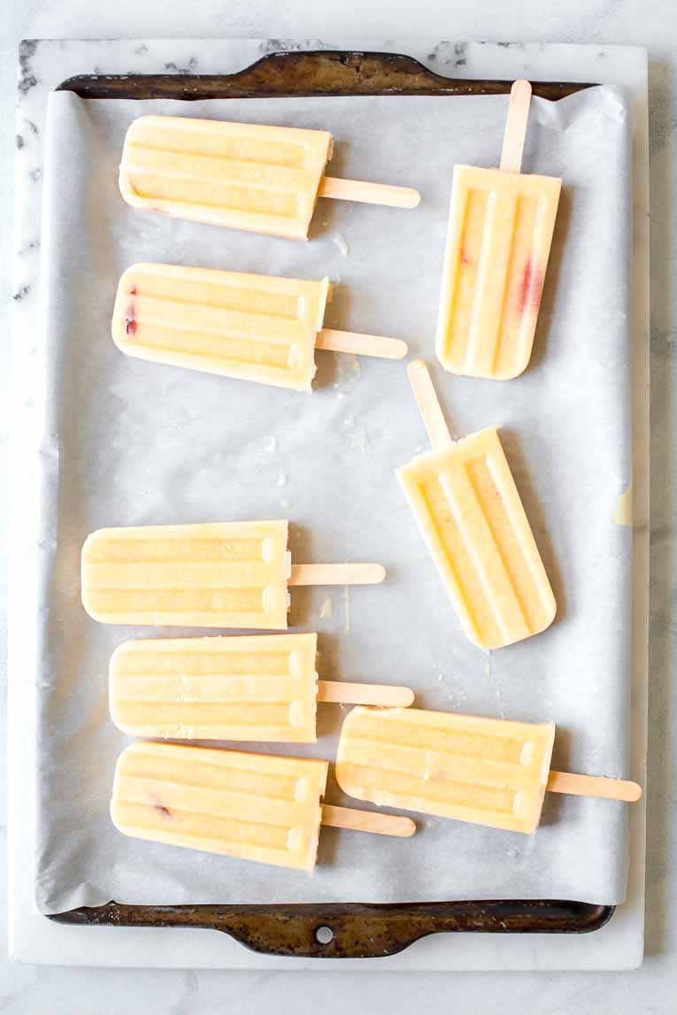 Frozen peach popsicles on a baking sheet with parchment paper.