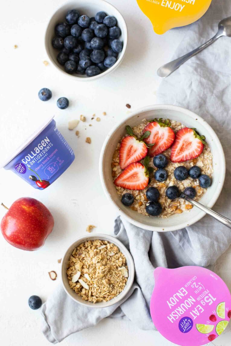 Bowl of oatmeal with fruit and granola next to yogurt cups.