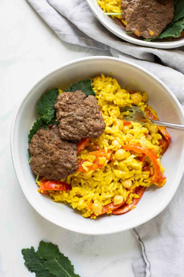 Two beef burger patties with kale and curry rice in a bowl.