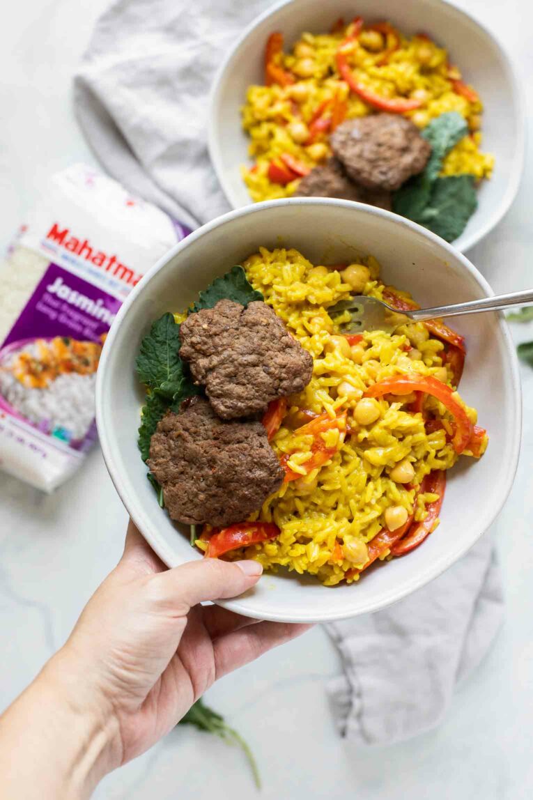 Hand holding Beef Curry Rice Burger Bowl with fork.
