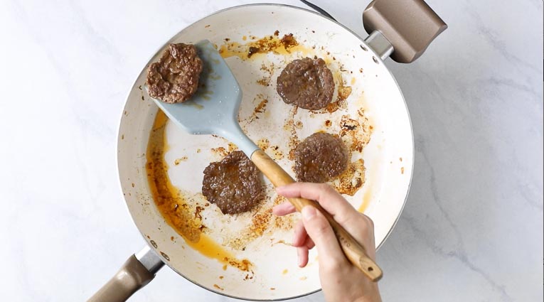 Burger patties being cooked in a white pan.