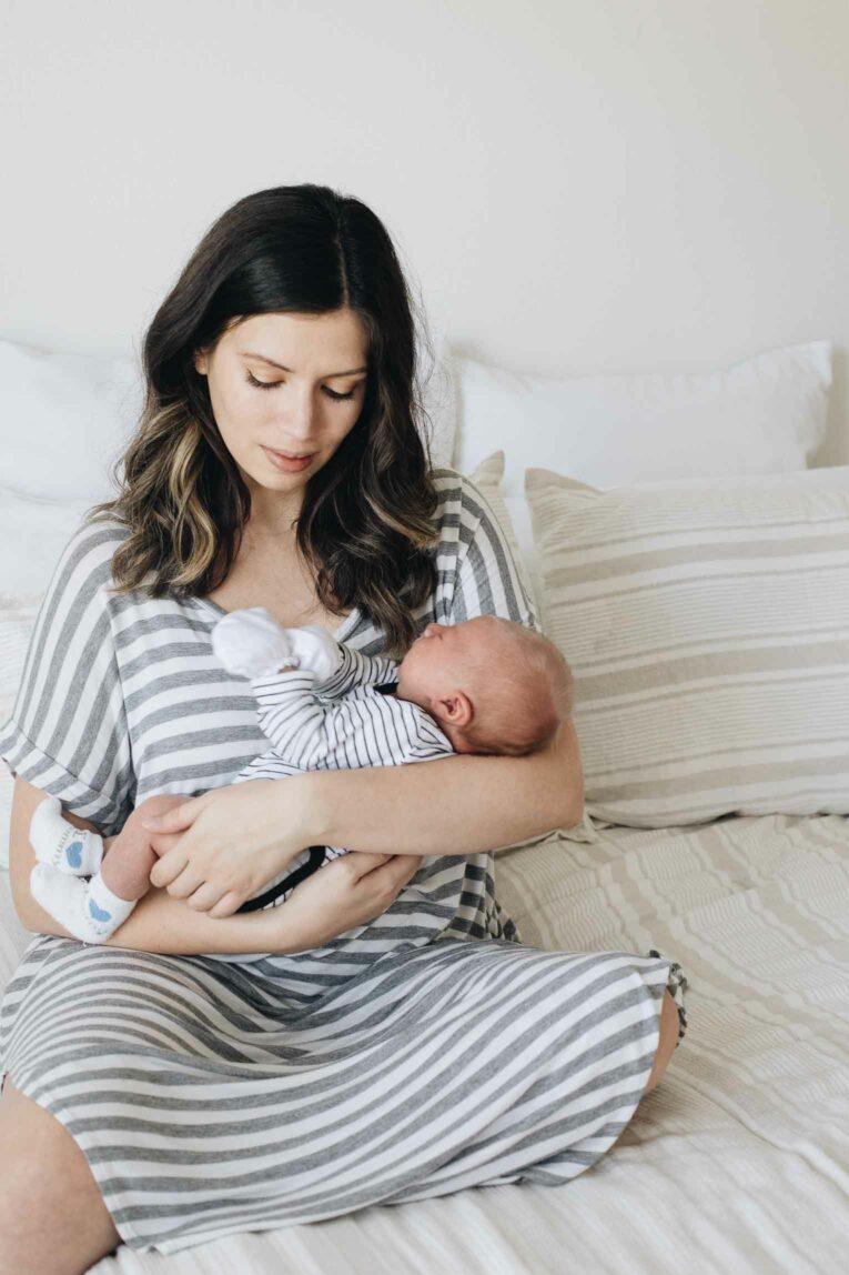 Mother holding baby in arms on bed.