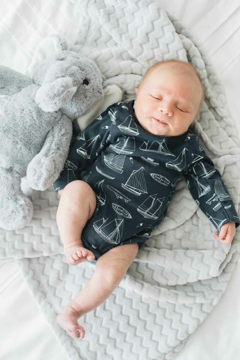 Newborn baby on a grey blanket with a stuffed animal.