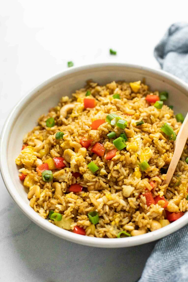 Angled shot of Thai Pineapple Fried Rice with a wooden spoon.
