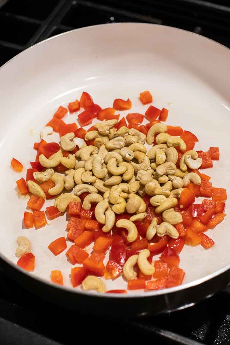 Peppers and cashews cooking in a skillet.