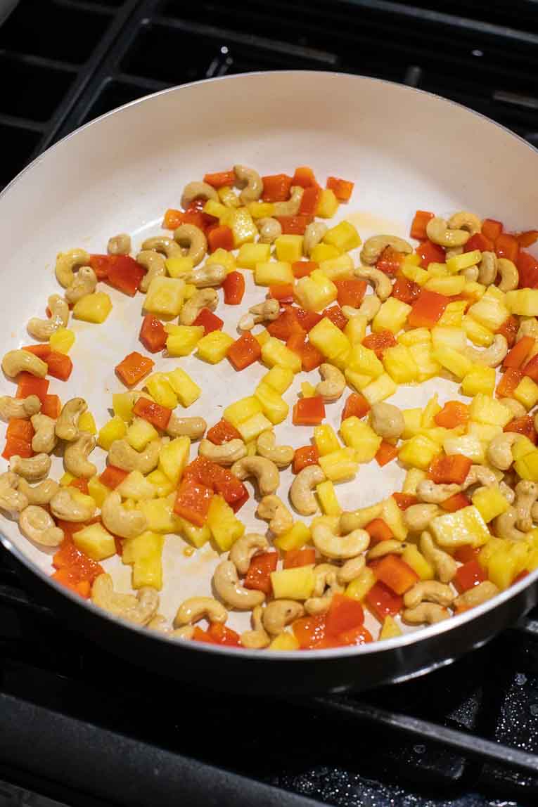 Pineapple, peppers, and cashews cooking in a white skillet.