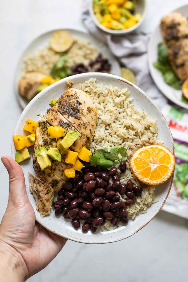 Hand holding plate of Cuban Mojo Chicken and Rice with black beans and salsa.