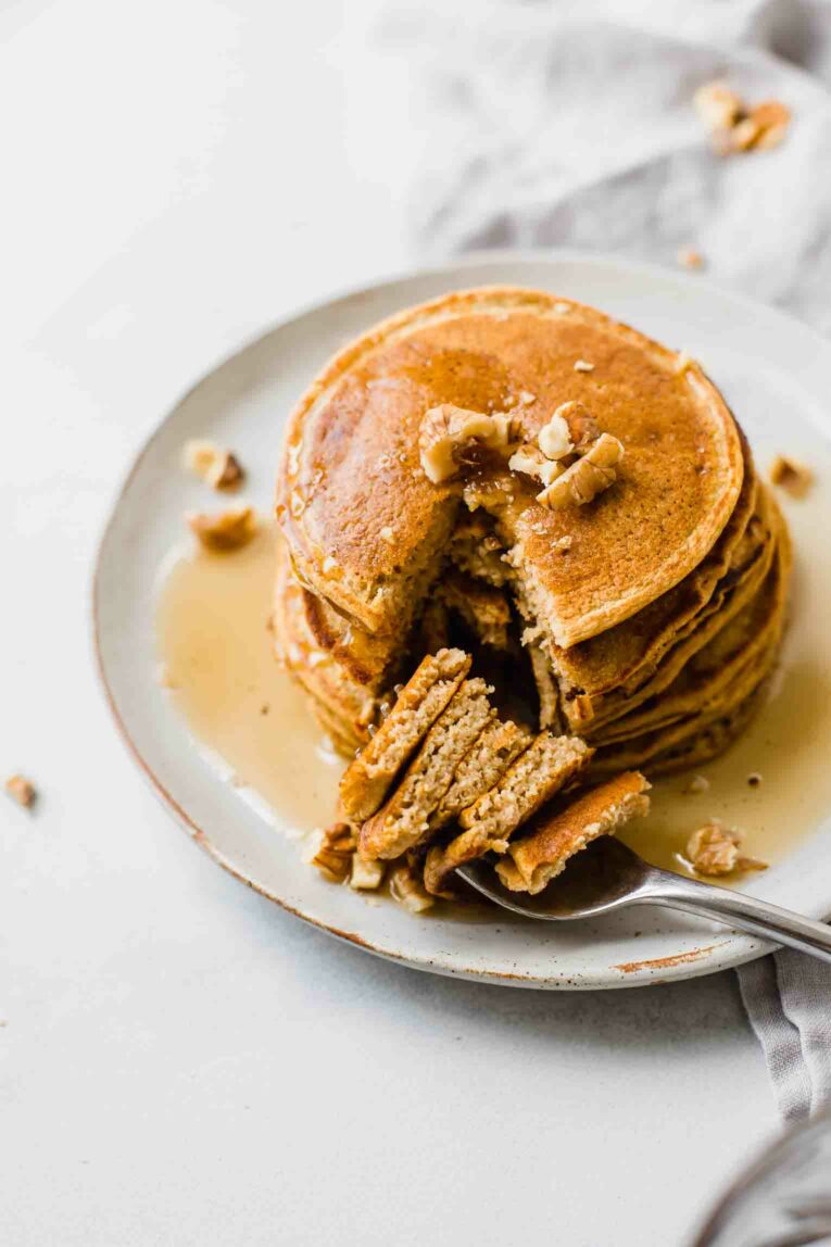 Fork cutting out a bite of sweet potato pancakes on a plate.