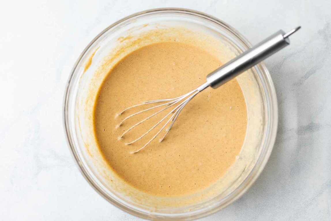 Pancake batter being whisked in a glass bowl.