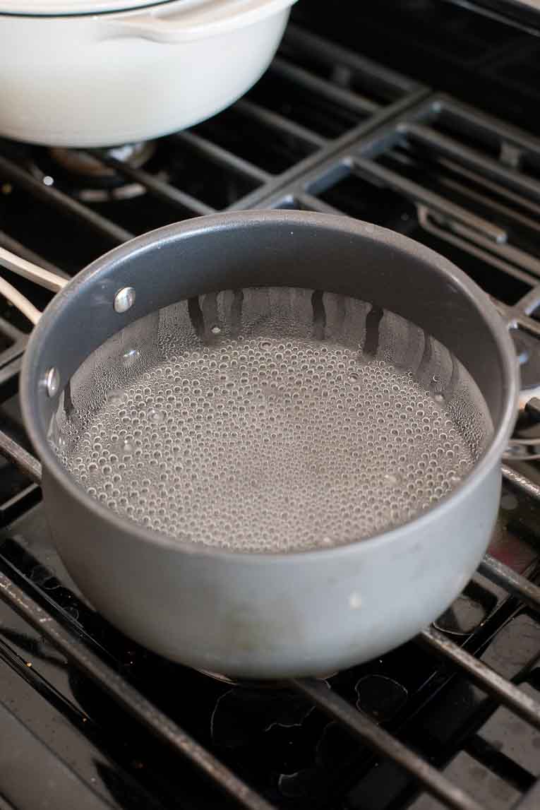 Pot of boiling water on a dark stove.
