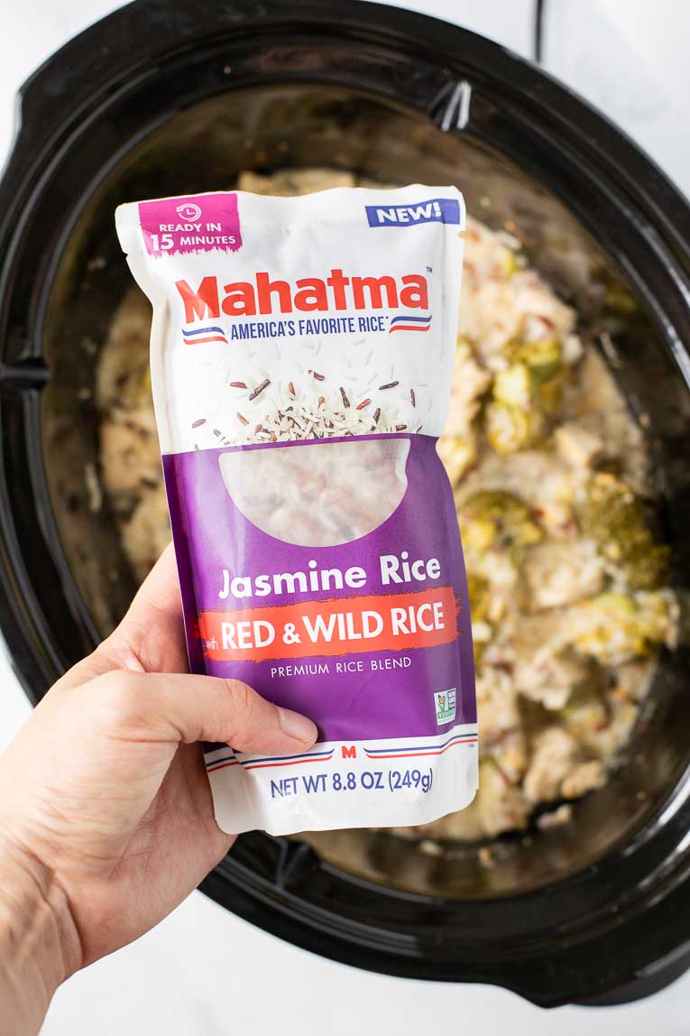 Hand holding Mahatma Rice over crockpot recipe.