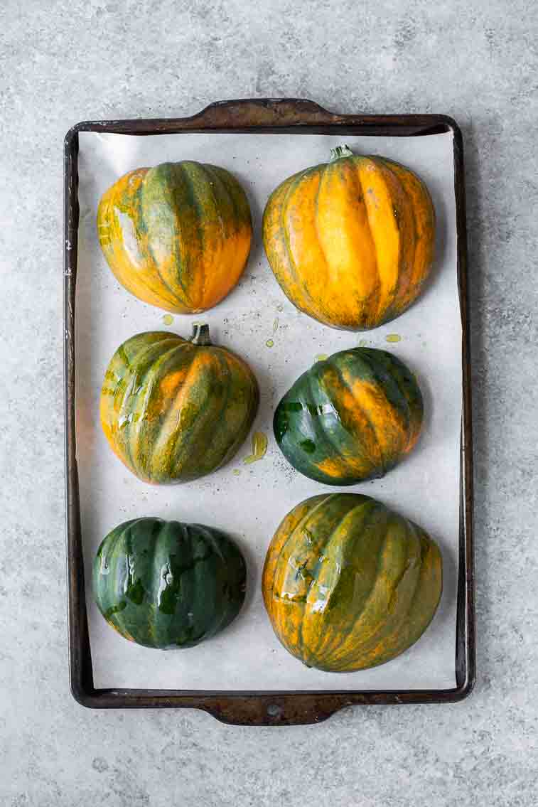 Raw acorn squash face down on a baking sheet.