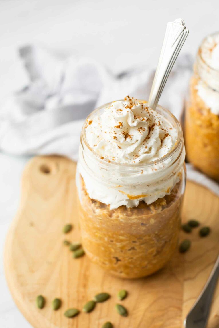 Angled shot of pumpkin pie overnight oats topped with coconut whipped cream.