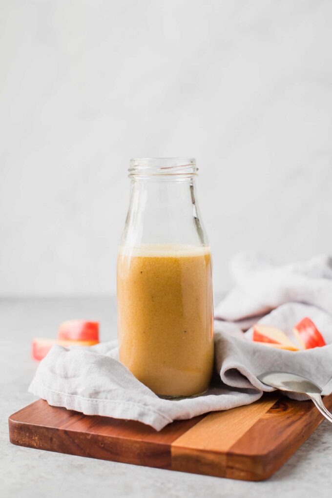 Apple cider vinaigrette in a glass bottle on a cutting board.
