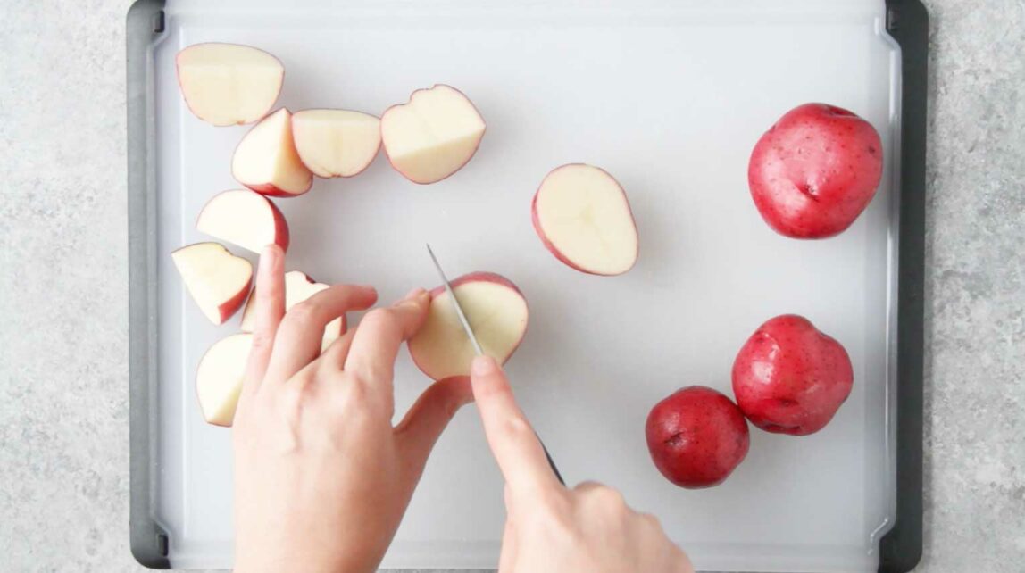 Hands cutting potatoes into quarters.