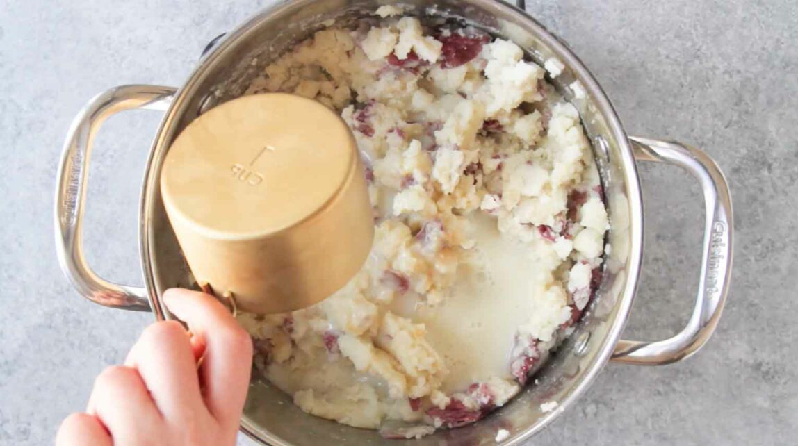Mashed red potatoes being mixed with milk.