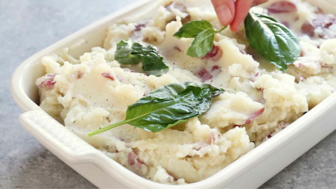 Mashed potatoes being topped with fresh basil.