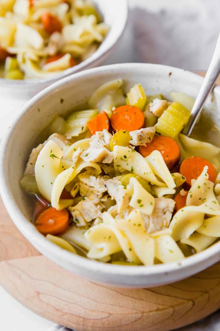Angled shot of turkey noodle soup in a white bowl.