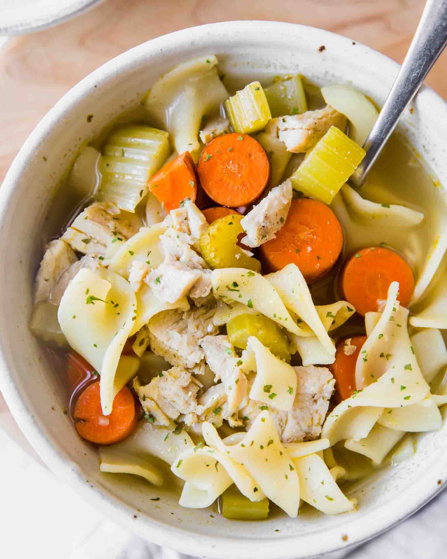 Top shot of easy turkey noodle soup in a white bowl with a spoon.