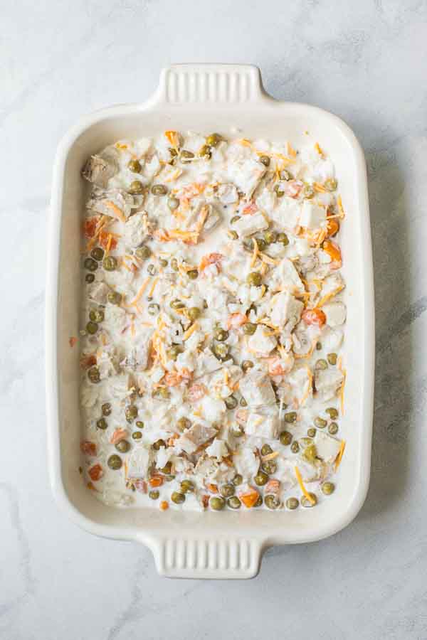 Rice, peas, carrots, turkey, creamy sauce, and cheese in a casserole dish.