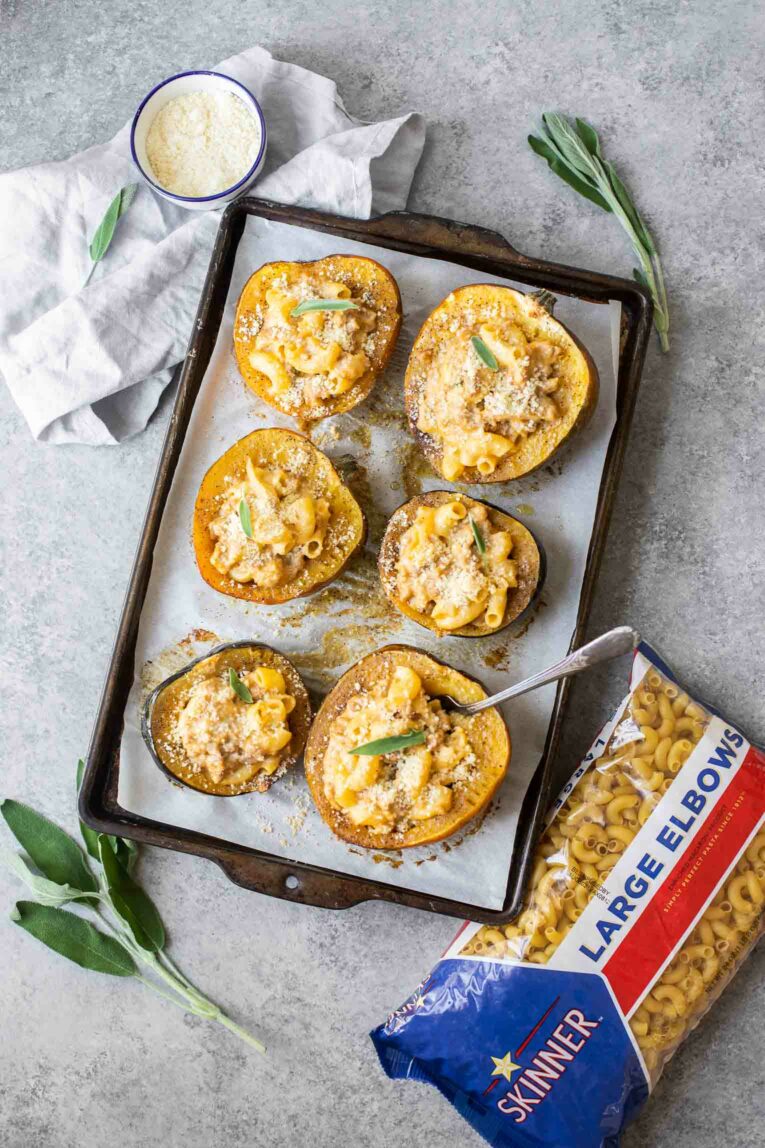Mac and cheese stuffed acorn squash on a baking sheet next to Skinner Large Elbows.