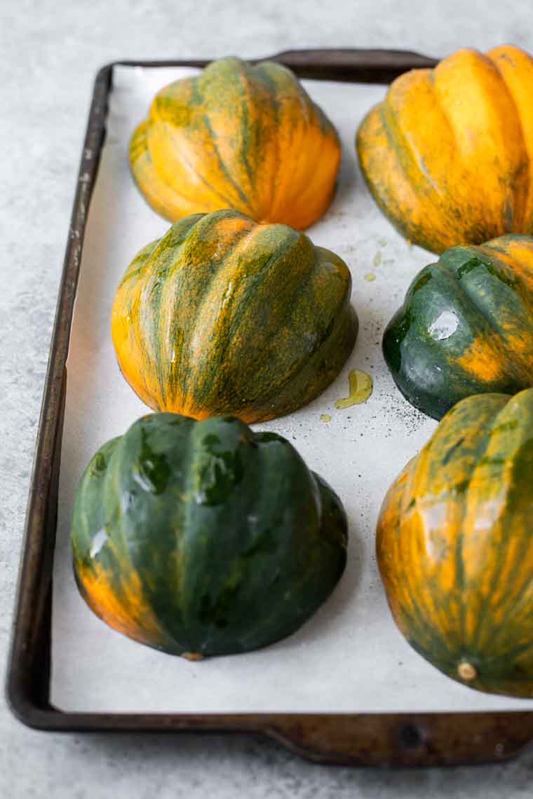 Halved acorn squash facedown on a baking sheet.