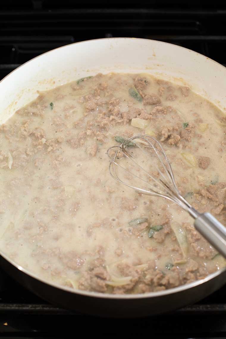 Milk being whisked into ground turkey and sage in a saucepan.