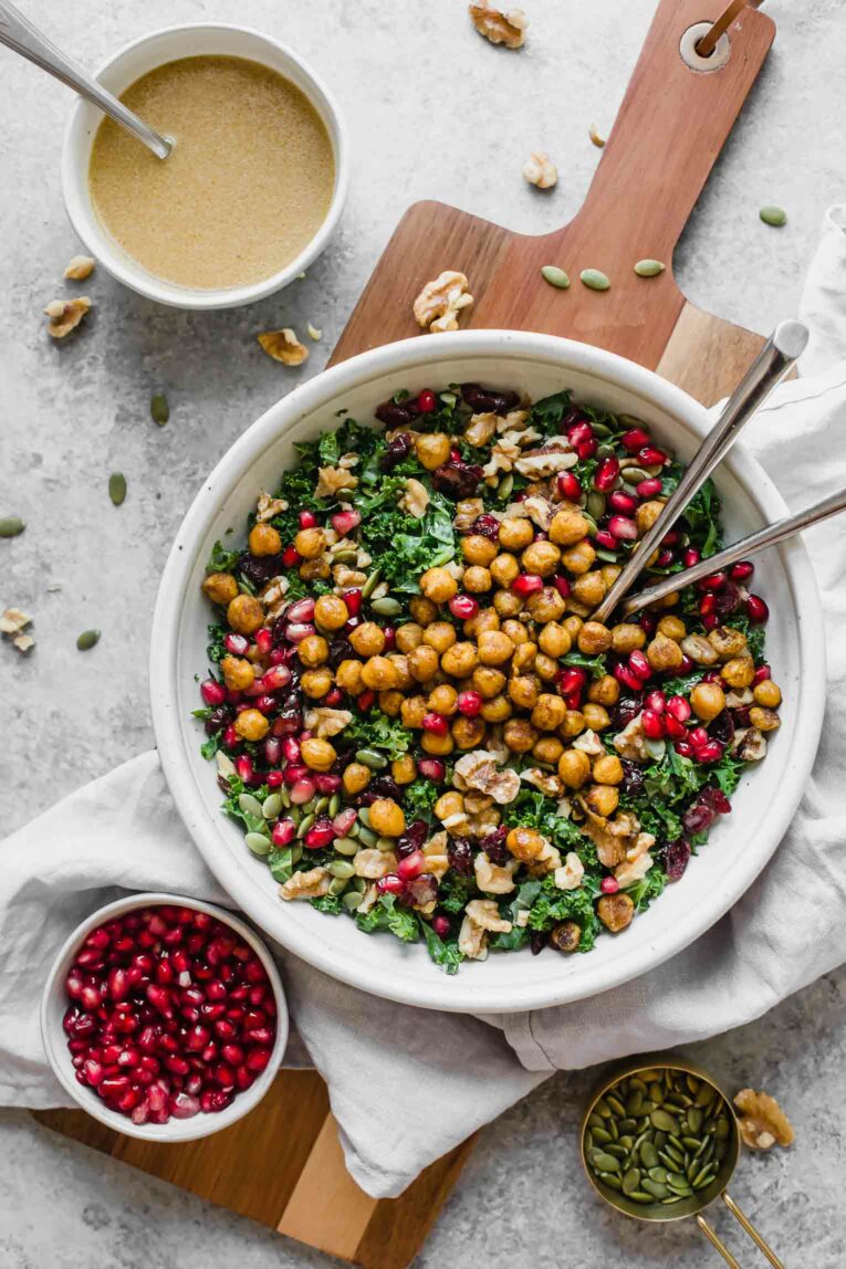 Styled top shot of a roasted chickpea fall salad in a white bowl with pomegranate arils and vinaigrette.