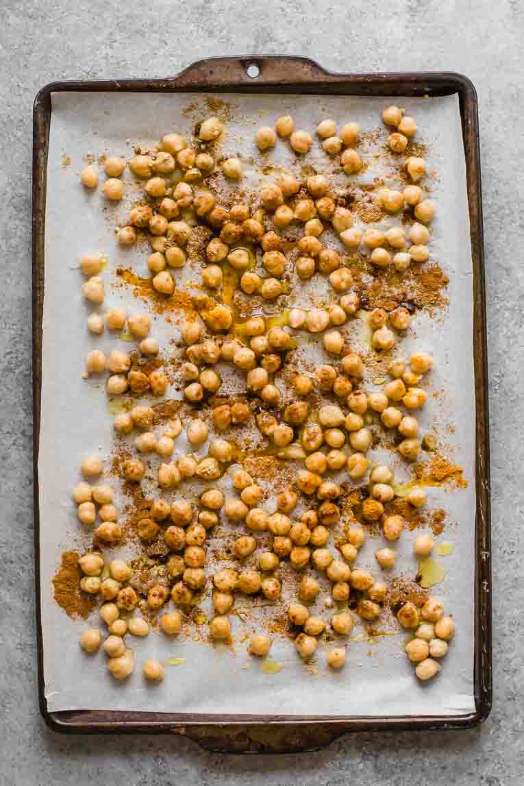 Chickpeas with tandoori seasoning and olive oil on a baking sheet.