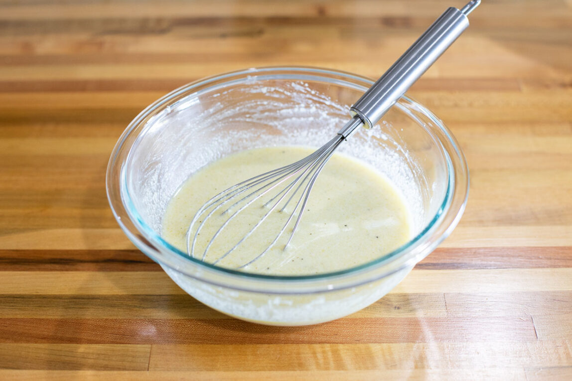 Creamy sauce being whisked in a glass bowl.