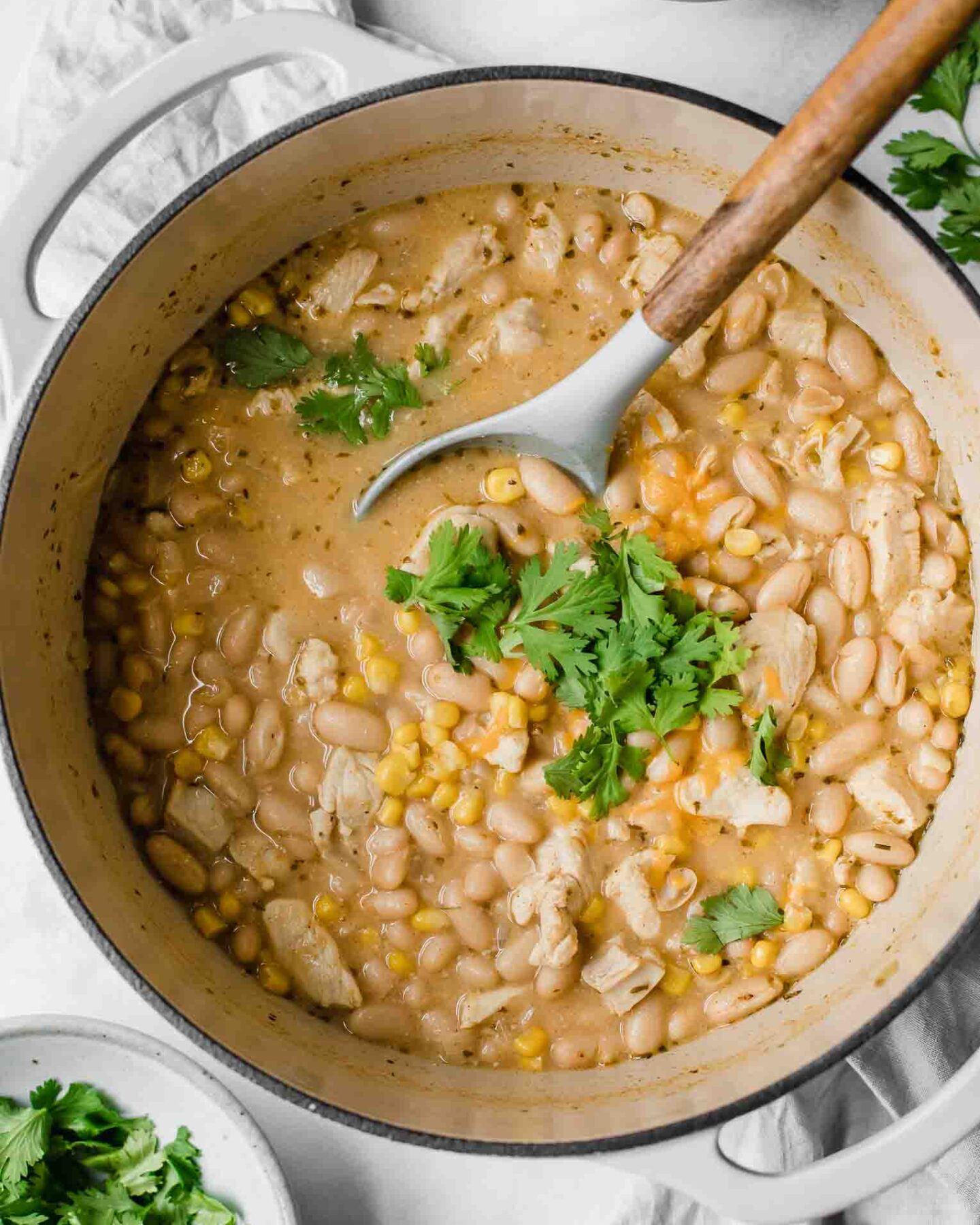 Creamy white chicken chili topped with cilantro and cheese in a dutch oven.