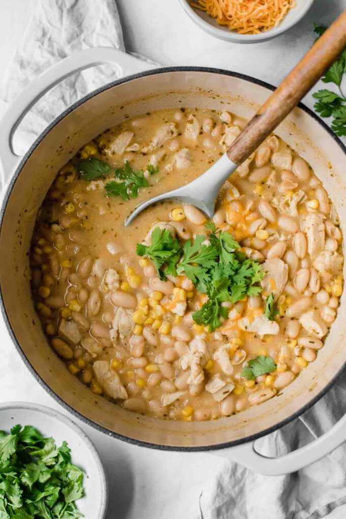 Creamy white chicken chili topped with cilantro and cheese in a dutch oven.