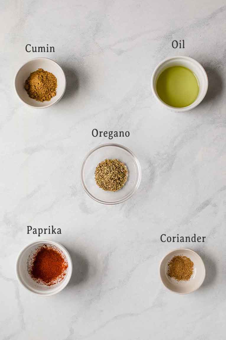 Spices used in white chicken chili on a marble table.
